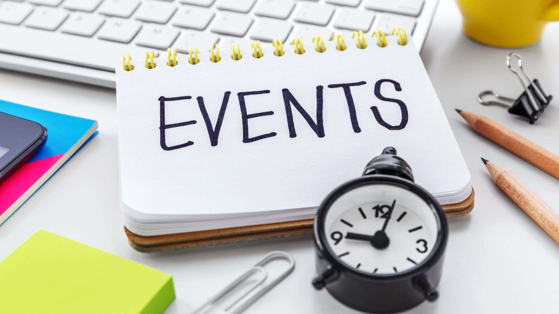 A notebook labeled 'EVENTS' next to office supplies and a clock, symbolizing the planning of events.